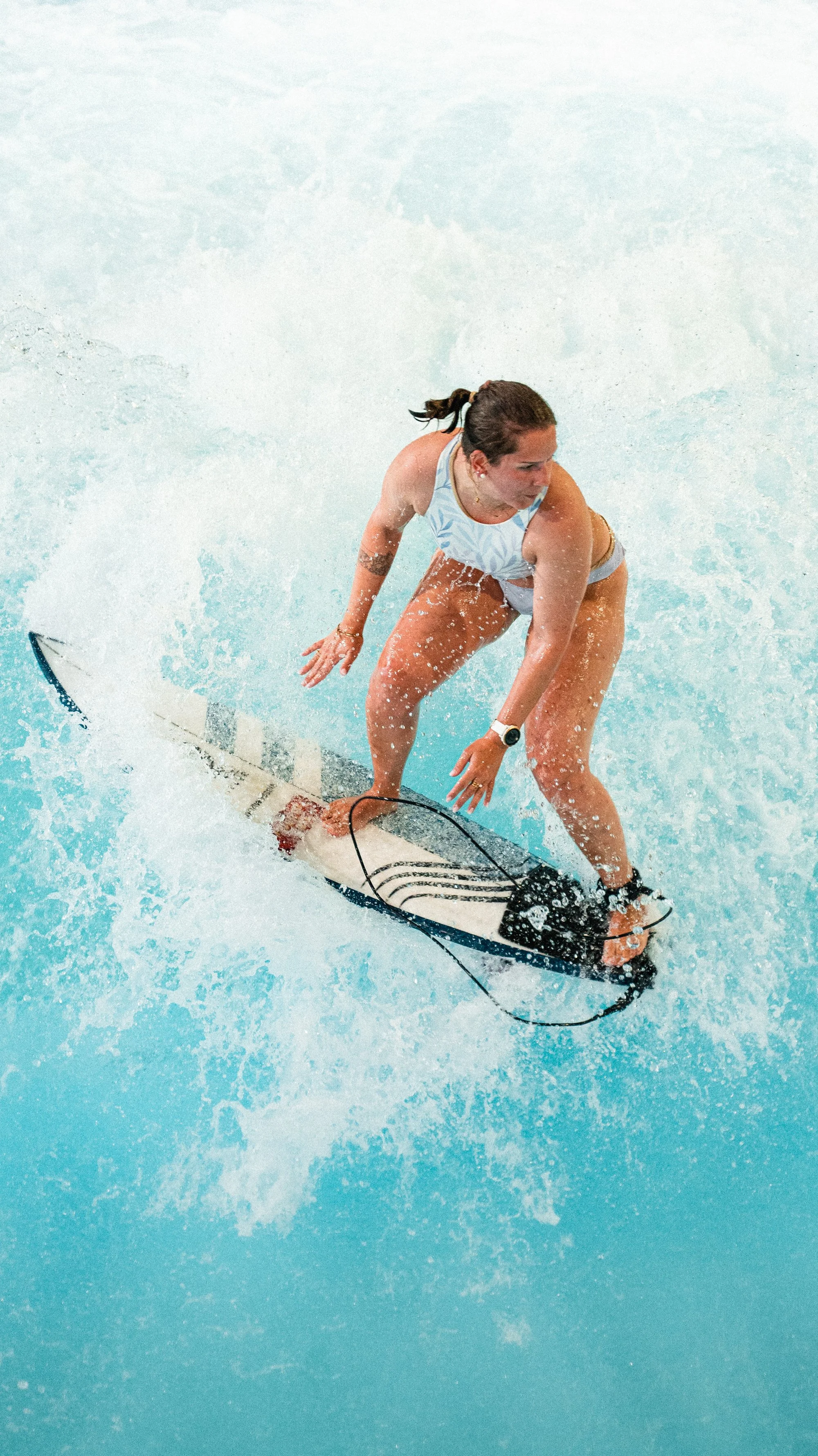 Une femme fait du skateboard aquatique dans une piscine, portant un maillot de bain sans manches et une montre.